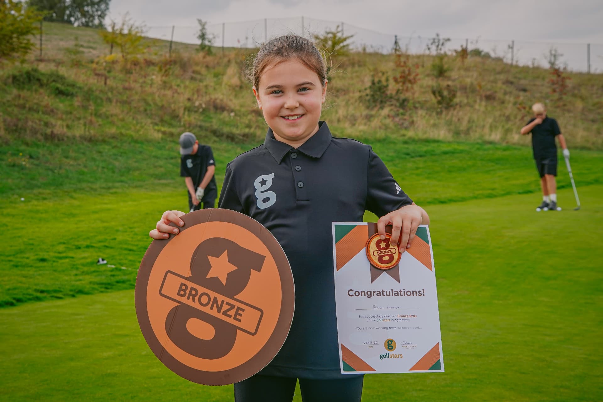 A junior golfer holding her Golfstars certificate on the course