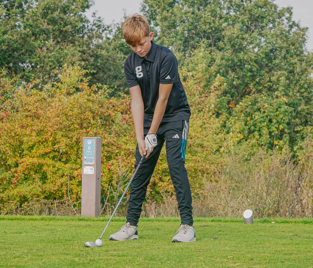 A golfstars player in black addressing the ball on the tee