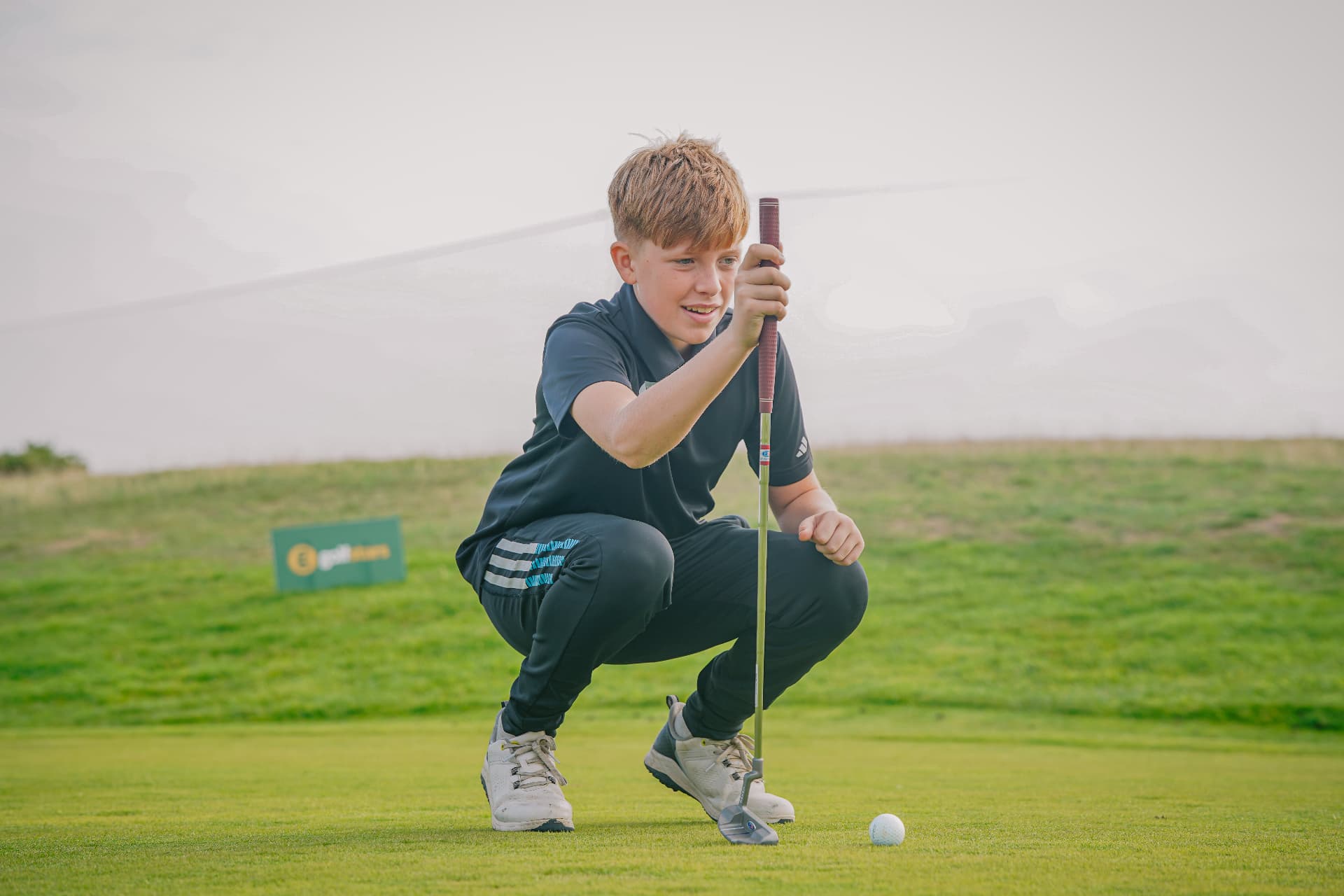 A golfstars player crouching to line up a putt on the green