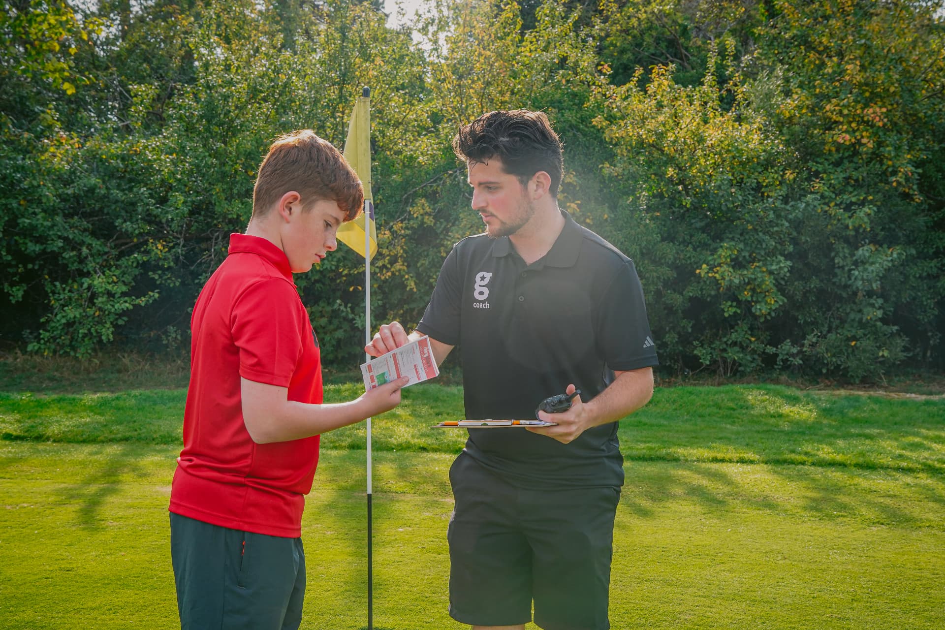 A Golfstars coach checking a young golfer's scorecard by the flag on matchday