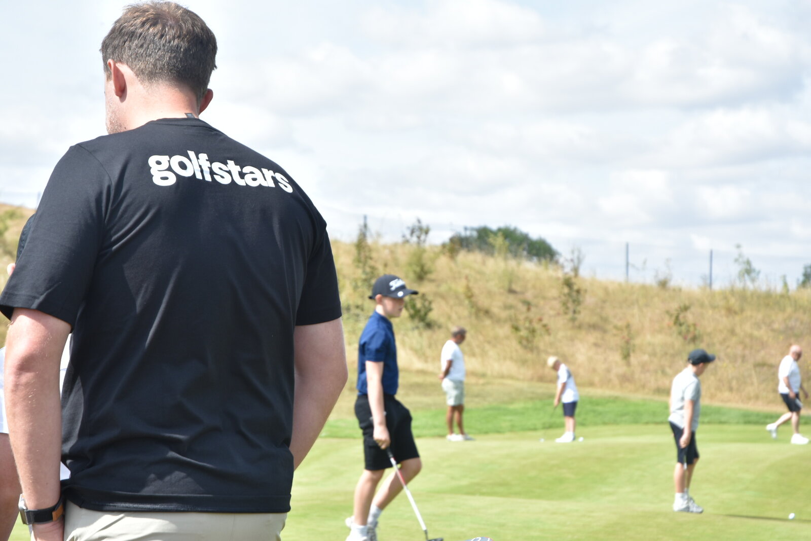 A Golfstars coach watching juniors practise on the putting green at camp