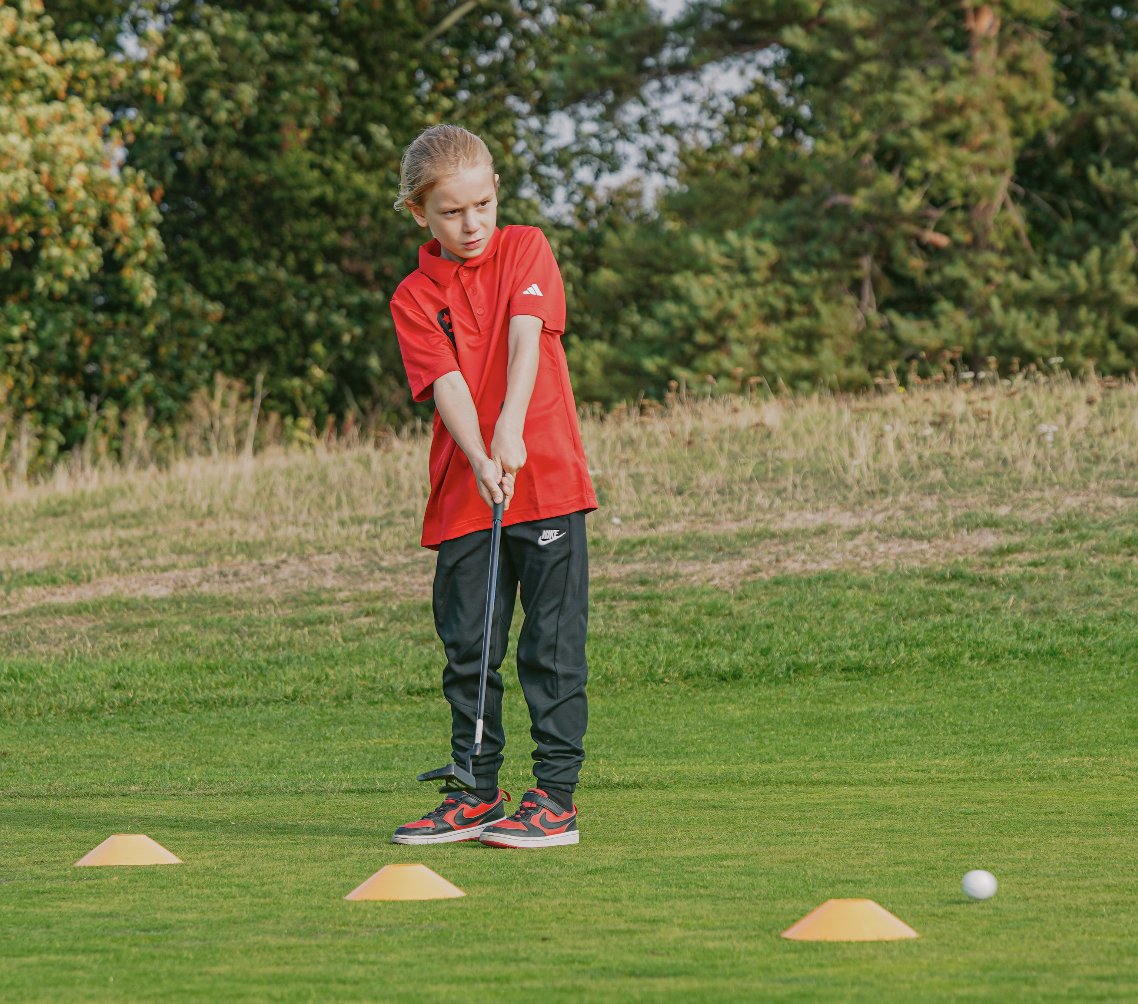 A young golfstars player in a red polo putting between practice cones