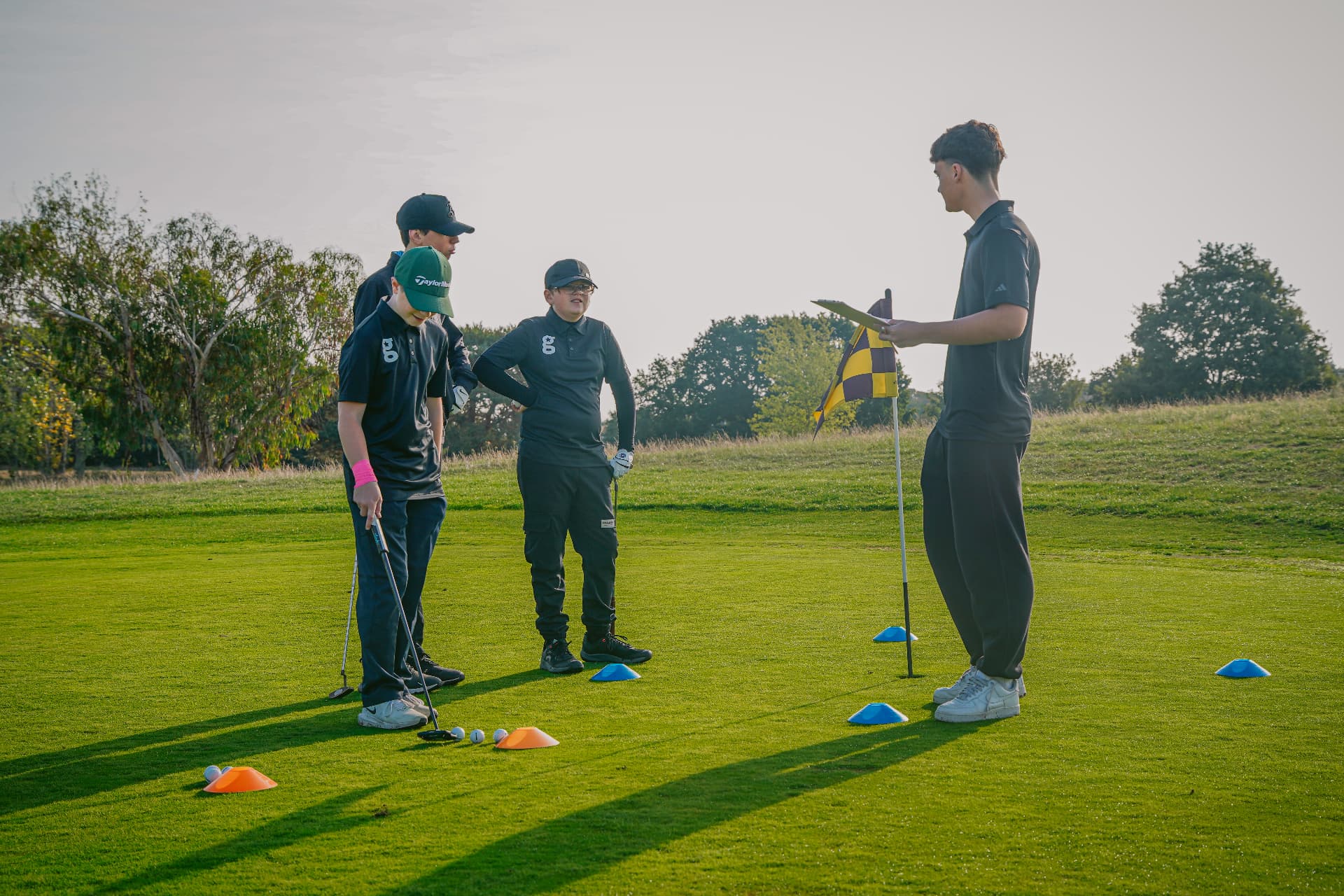 Golfstars players and their coach gathered around the flag on the practice green