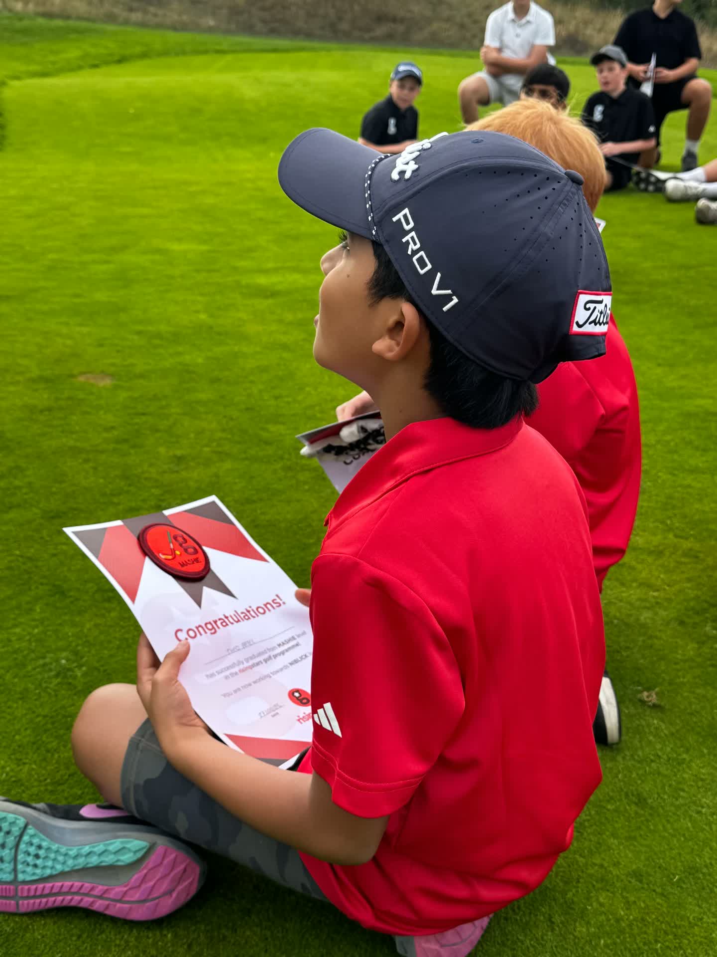A junior golfer holding his certificate and badge on the course