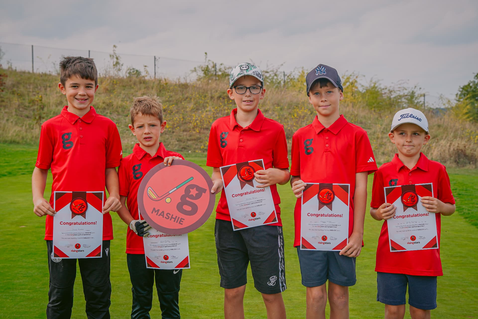 Five young golfers in red Golfstars polos holding their Mashie graduation certificates