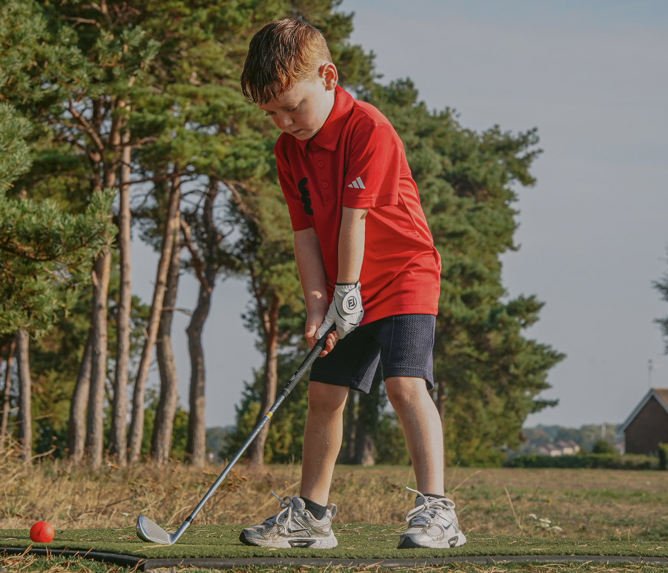 A young golfstars player in a red polo addressing the ball on a practice mat