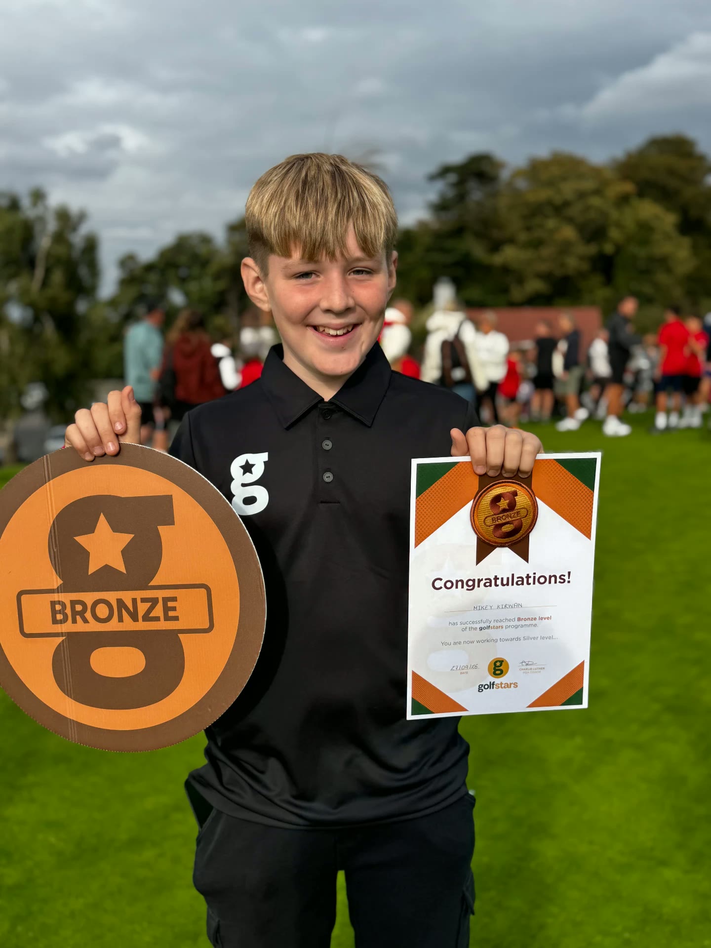 Smiling golfstars junior holding his Bronze badge and certificate