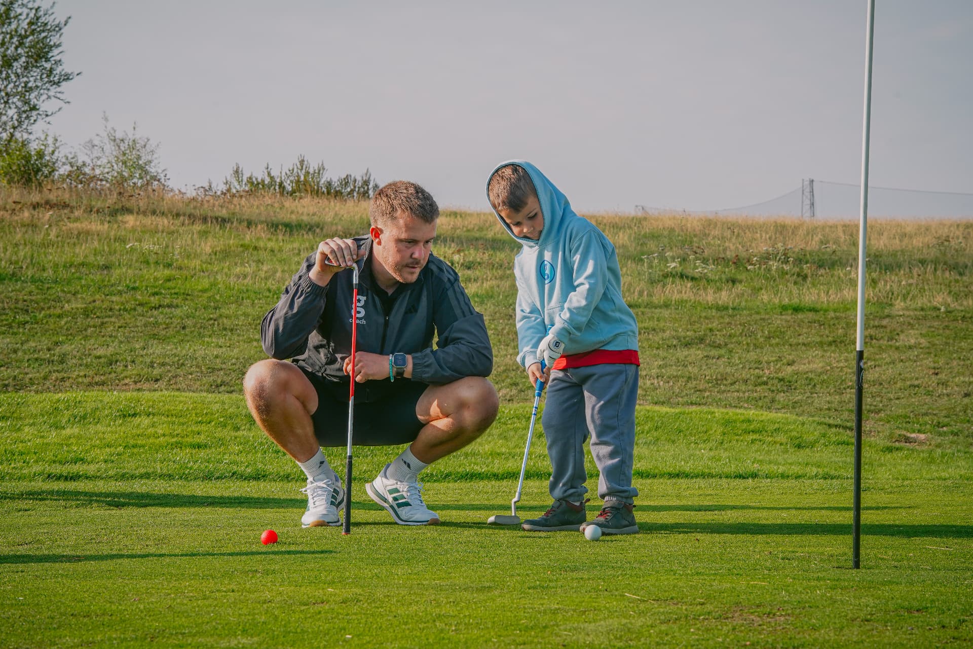 Golfstars coach helping a young golfer putt on a community golf green