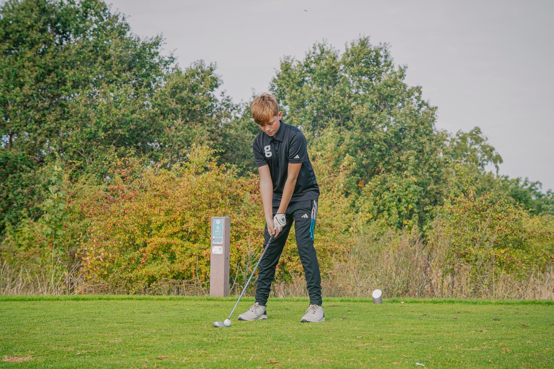 A golfstars junior in black addressing his ball on the tee
