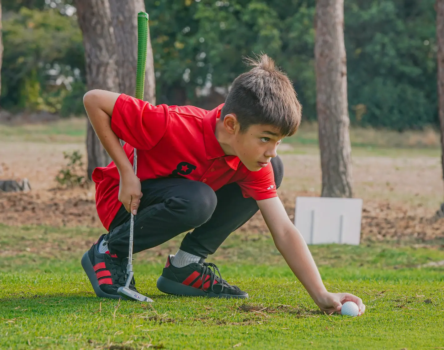 A young golfstars player crouching to mark his ball on the green