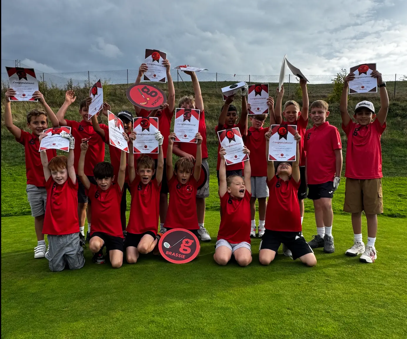 Junior golfers in red golfstars kit celebrating with their certificates on the green at Chadwell Matchday