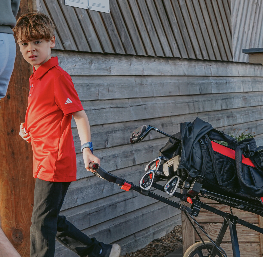 A young golfstars player in a red polo pulling his golf trolley