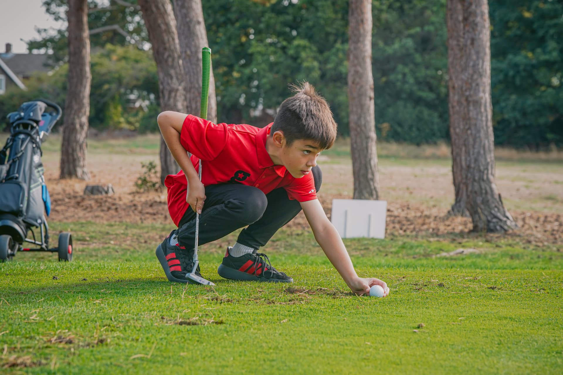A young golfstars player in red marking his ball on the green