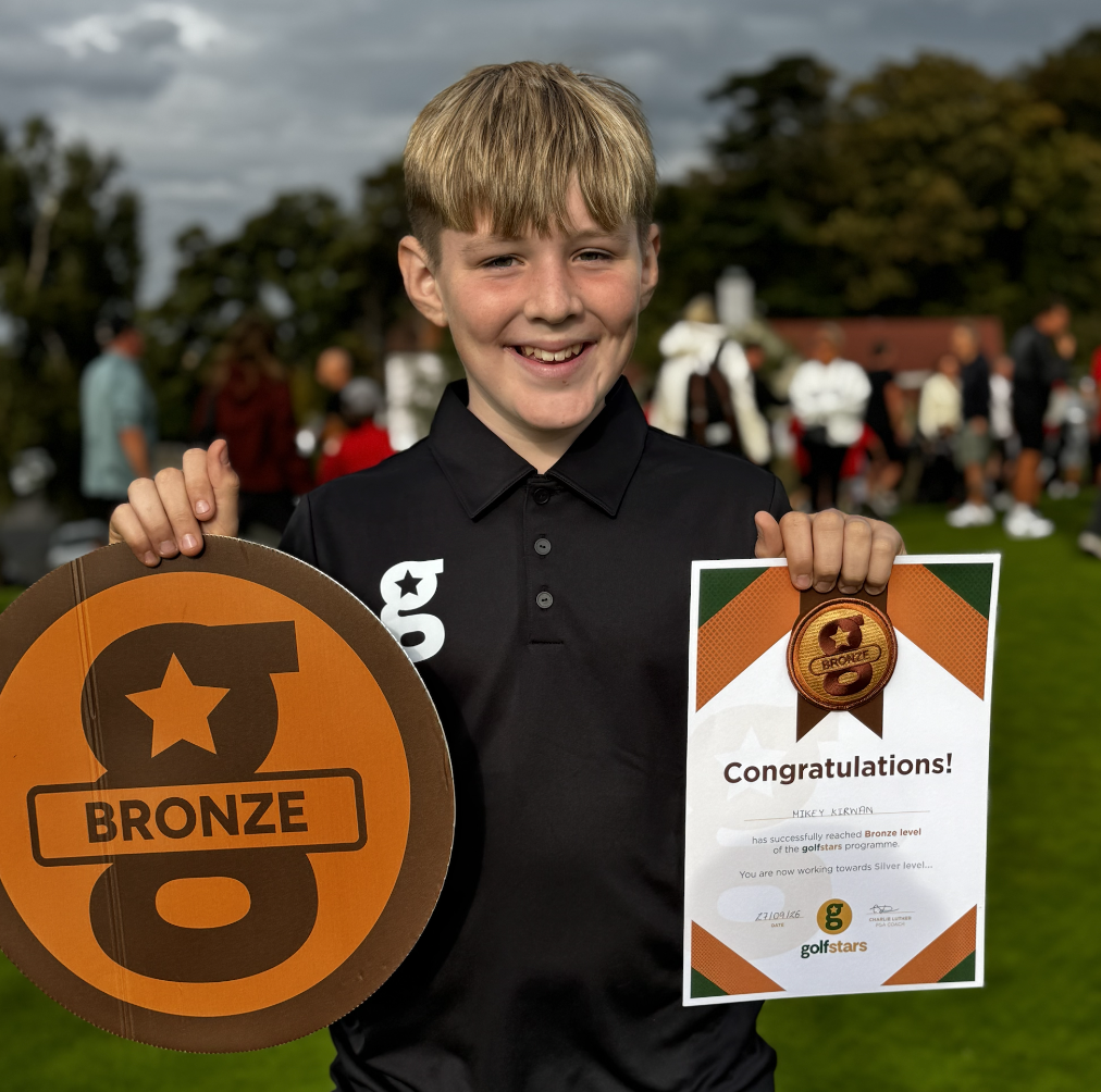 A smiling young Golfstars golfer holding his Bronze level badge and certificate on league day
